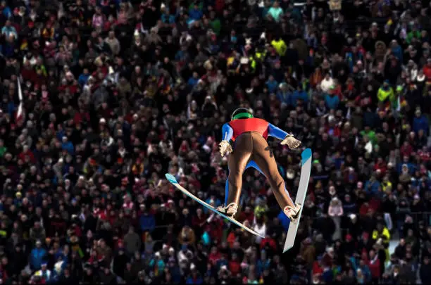 Young man jumping on the large hill, audience watching
