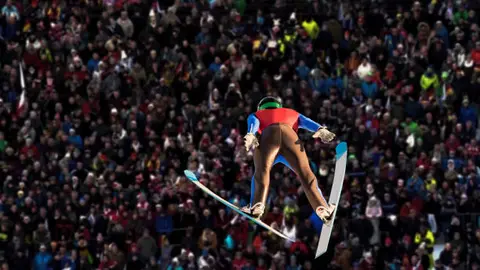 Young man jumping on the large hill, audience watching